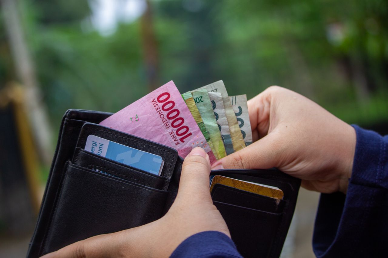 Rupiah Terlemah di Asia Saat Dolar Justru Melemah Close-up of hands holding Indonesian rupiah notes in a wallet outdoors.